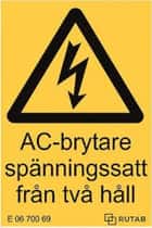 Bilden visar en gul varningsskylt med symbol för elektrisk fara och texten ”AC-brytare spänningssatt från två håll”. Skylten varnar för att brytaren kan ha ström från flera riktningar. Den används för att informera om risk vid arbete på en solcellsanläggning. Texten och symbolen visar tydligt att försiktighet krävs vid hantering av brytaren.