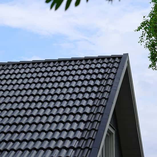 Ett tak med svarta tvåkupiga tegelpannor syns mot en blå himmel, där tunna svarta Wave-solpaneler ligger ovanpå och följer pannornas vågiga form.