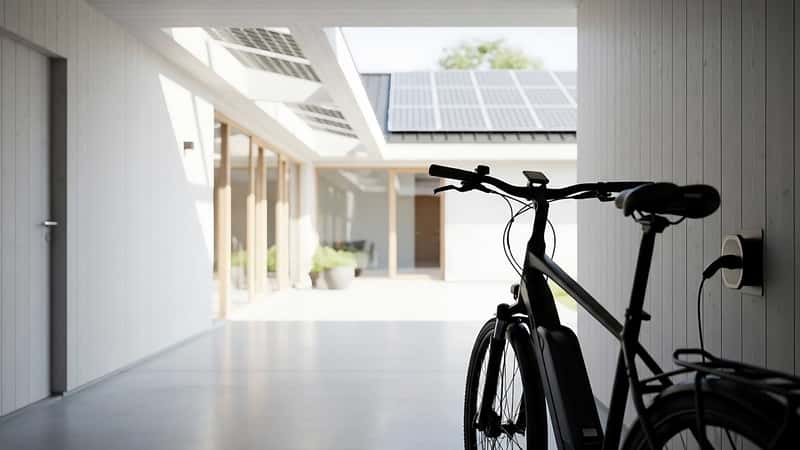 En elcykel laddas med energi från solpaneler på ett modernt hus.