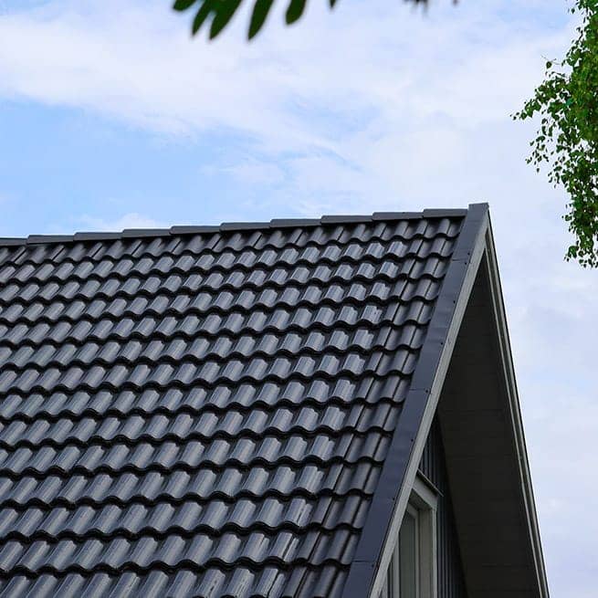 Ett tak med svarta tvåkupiga tegelpannor syns mot en blå himmel, där tunna svarta Wave-solpaneler ligger ovanpå och följer pannornas vågiga form.