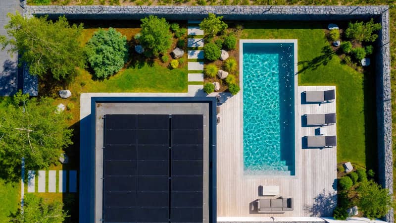 Luftfoto över solpaneler på platt tak bredvid en pool i modern trädgård, som visar hur solceller kan värma poolen.